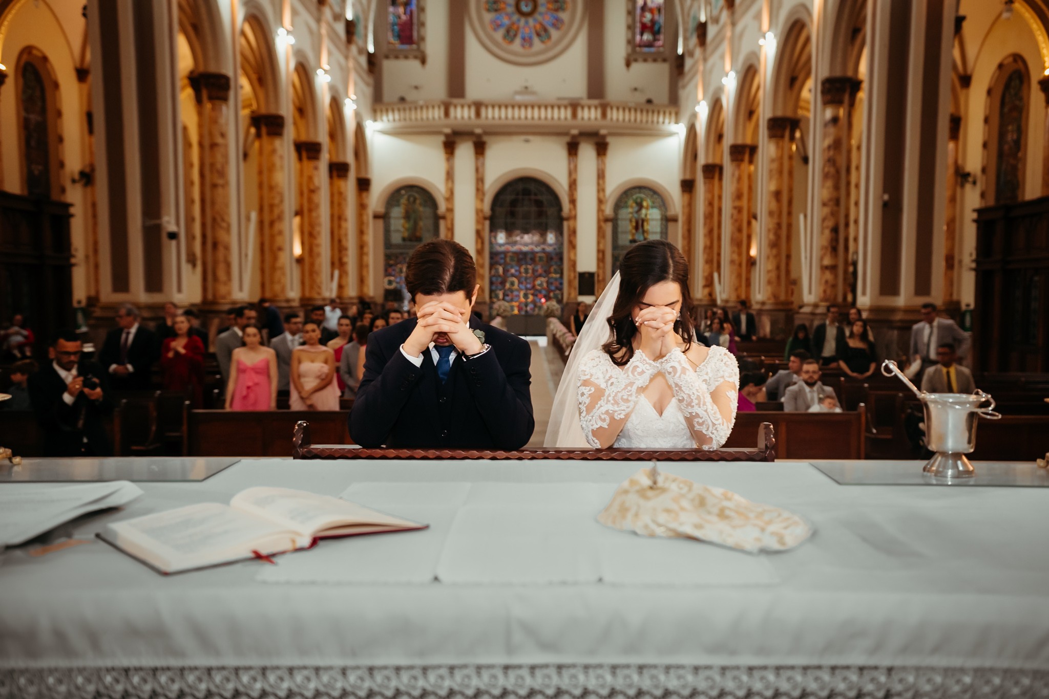 Casal ajoelhado em comunhão com a igreja ao fundo
